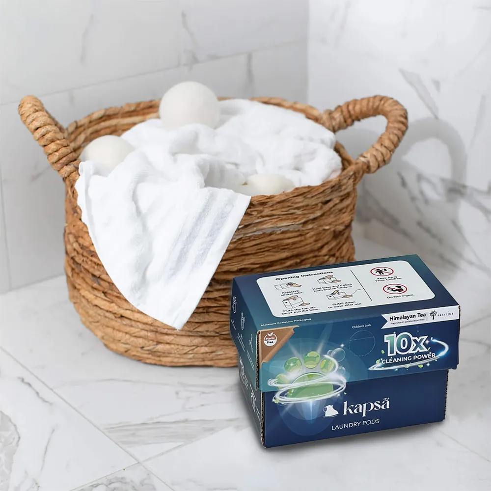 A box of Kapsä laundry pods beside a basket of fresh white towels