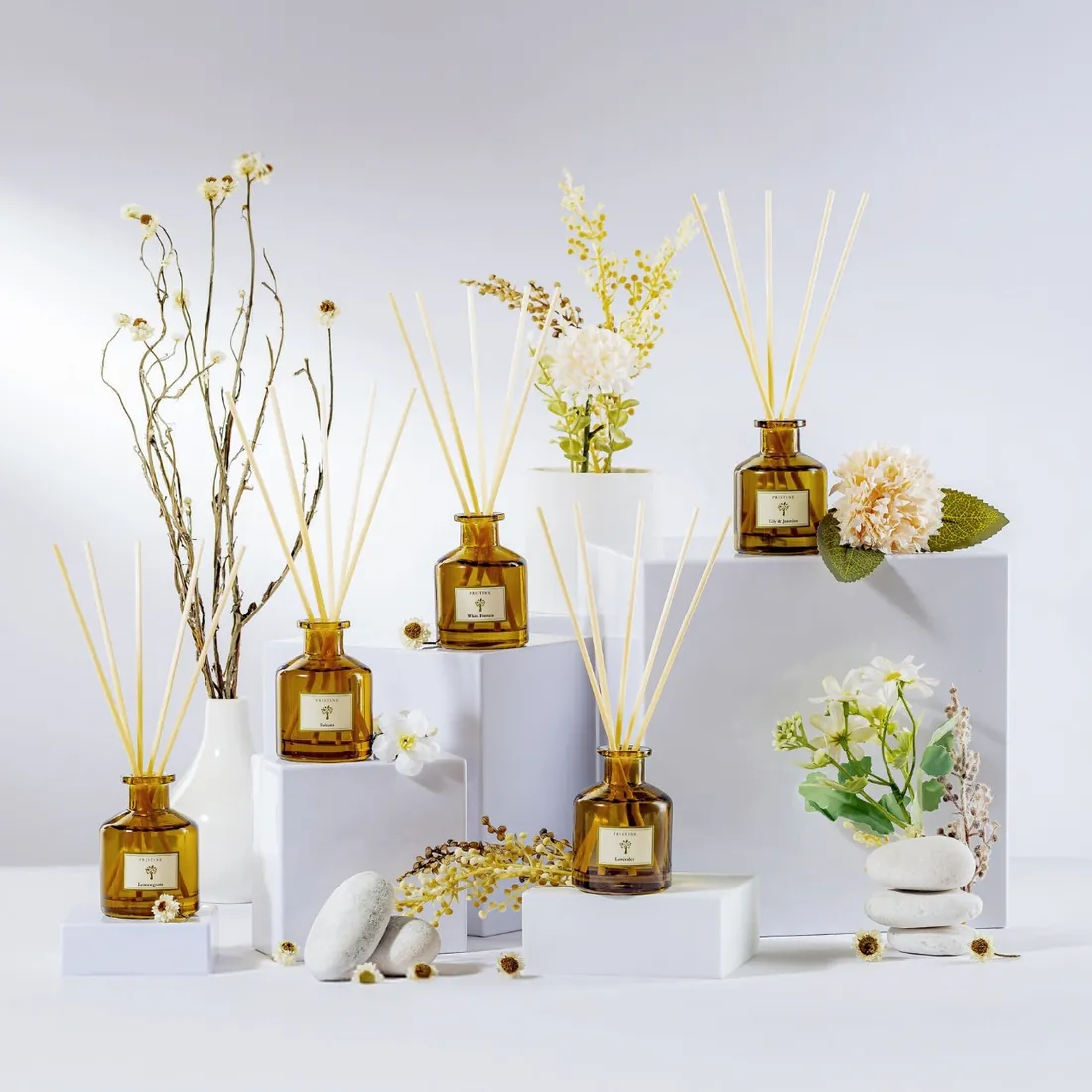 Pristine reed diffusers arranged with dried flowers on white plinths